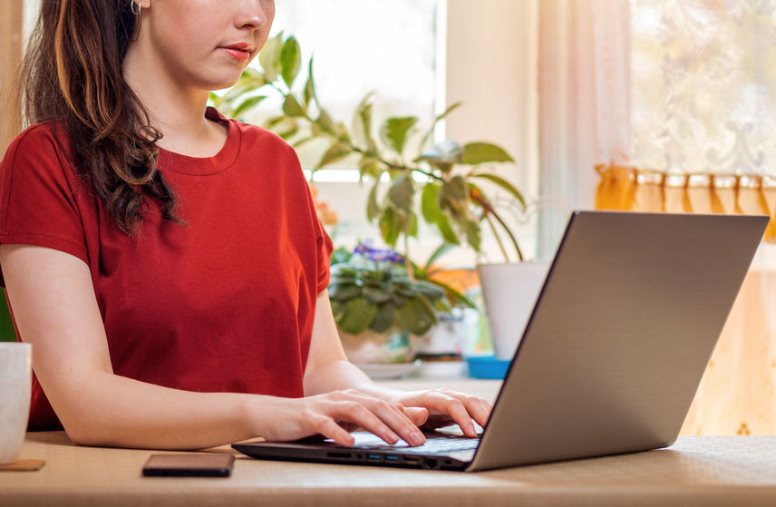 Freelance.A young, pretty woman is typing on a laptop while sitting at her Desk. Home decor, the sun outside the window. Close up. The concept of quarantine, self isolation and remote work